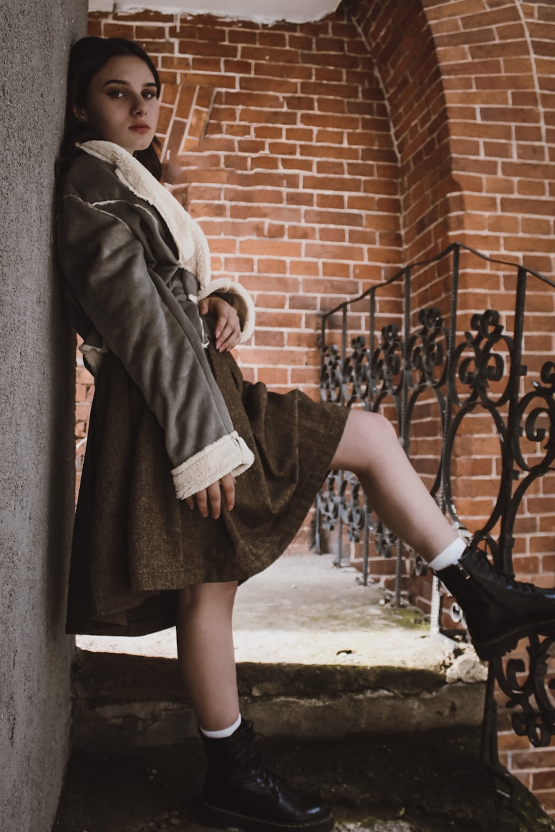 woman in gray coat and black skirt standing beside black metal fence during daytime