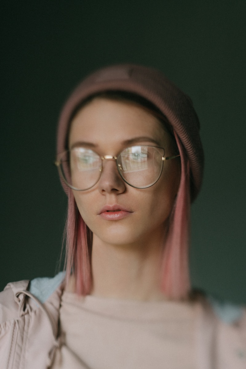 A woman with pink hair wearing glasses and a hat